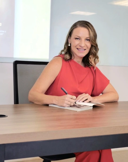 Gisele Mendonça, psicóloga e hipnoterapeuta, sentada à mesa com um caderno.